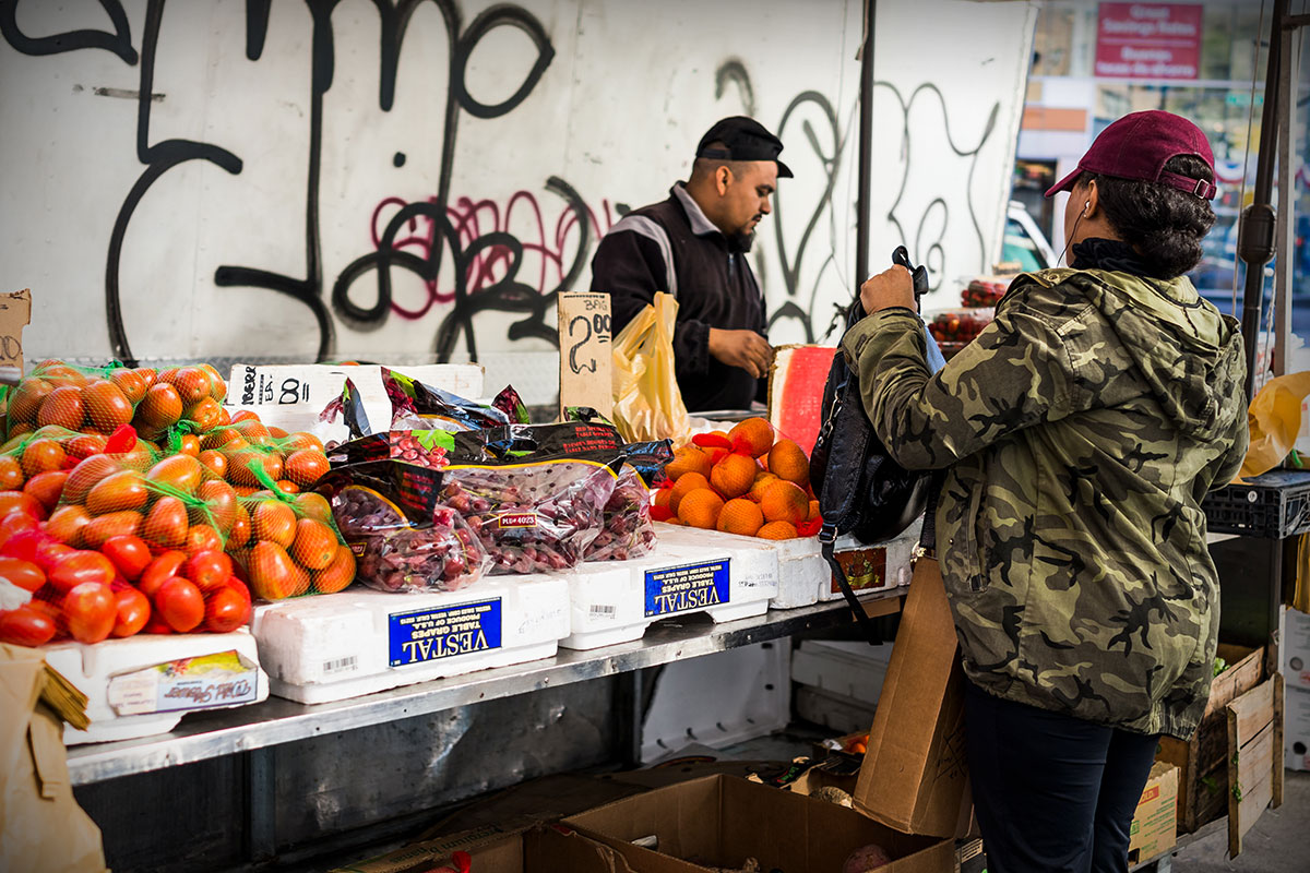 A street-side vendor sells fresh fruit and vegetables to a customer. 