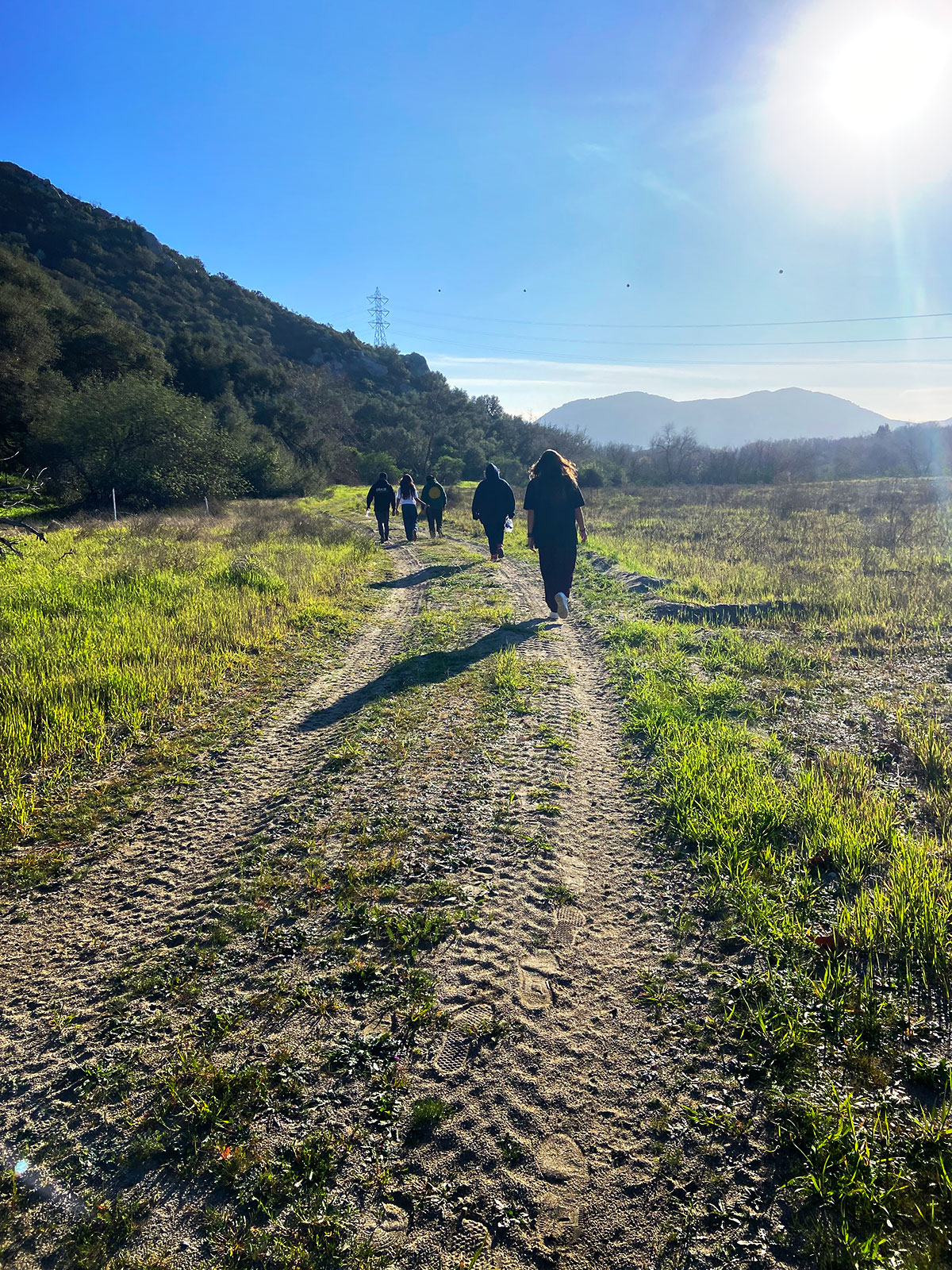 Group of people walking down dirt path under a blue sky