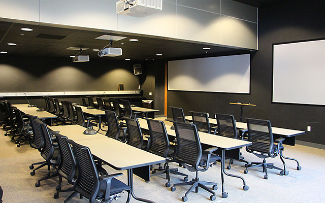 30 chairs arranged behind long tables and facing 2 screens